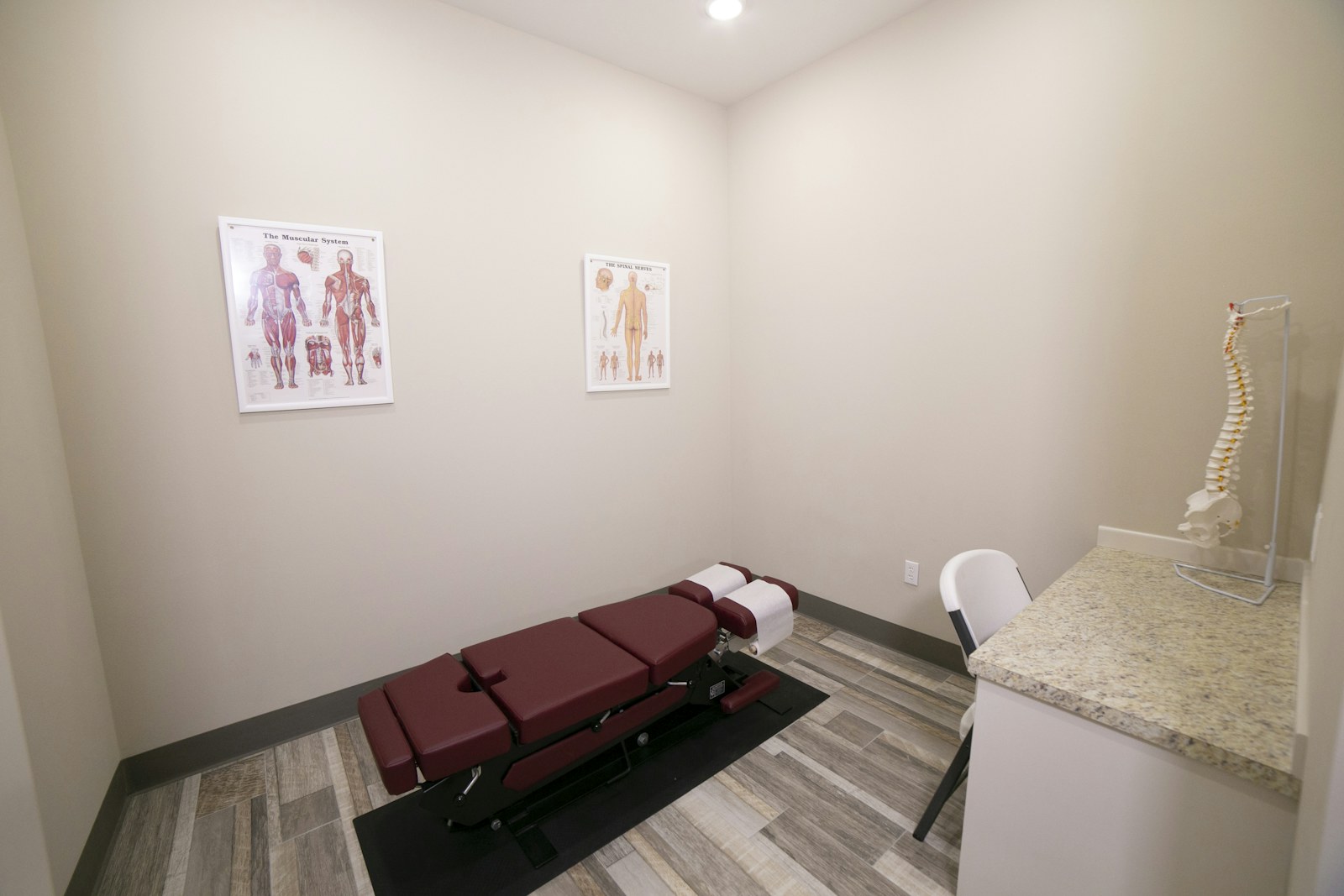 Chiropractic adjusting table in a treatment room with anatomy charts